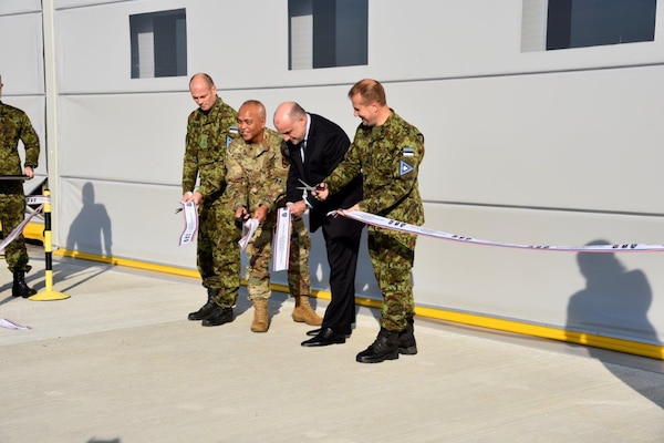 Four men stand in front of a building and cut a ribbon.