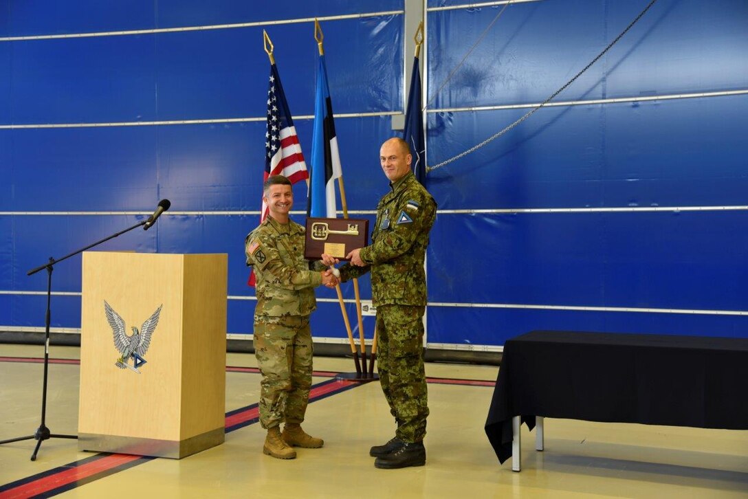 Two men stand, shaking hands and holding a plaque with a gold key.