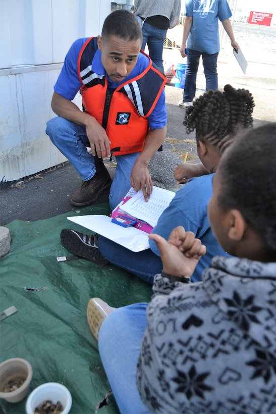 Man is life vest kneels by two little girls helping them do the math for their scientific process project.