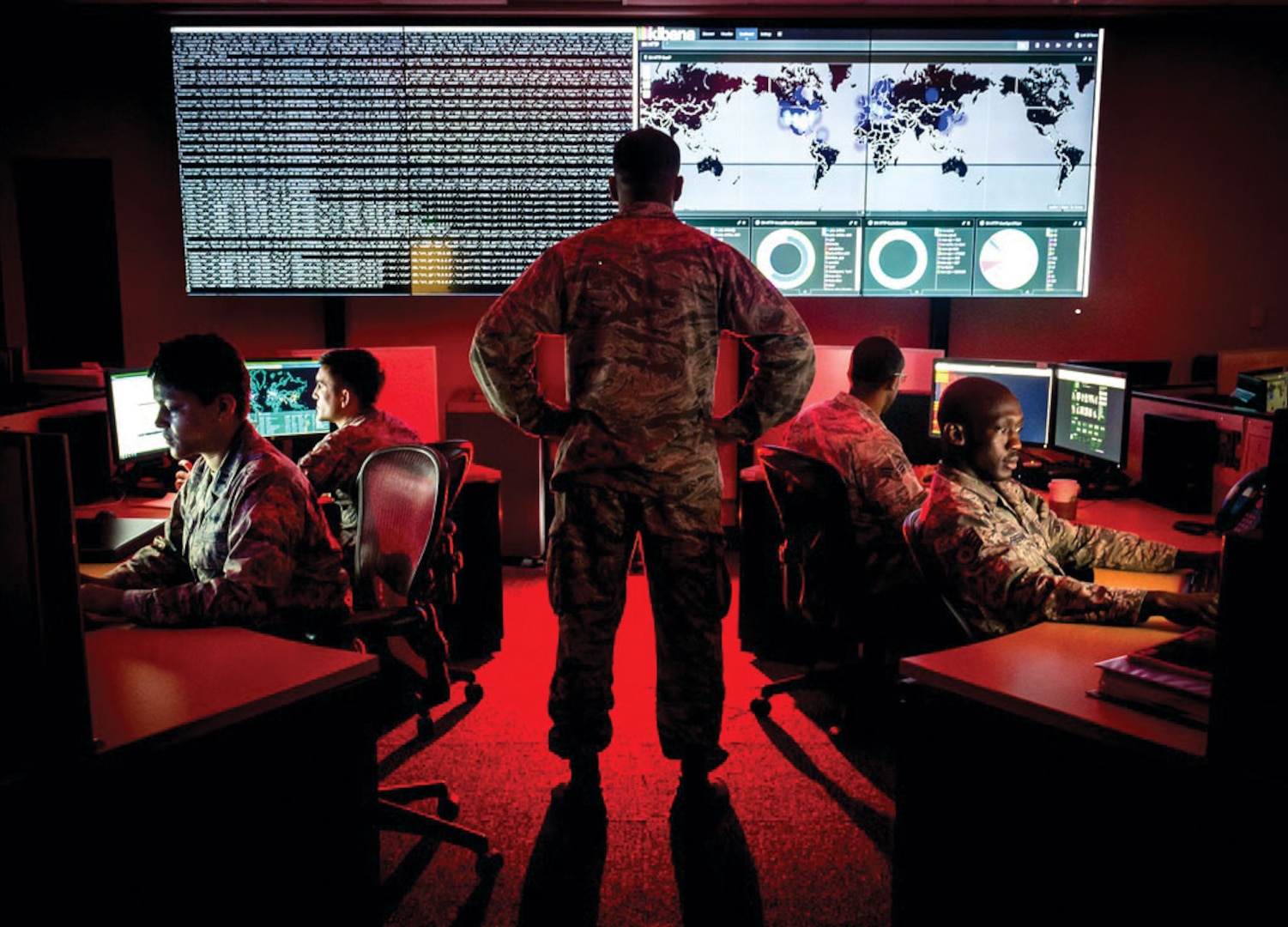 A cyber warfare operations officer reviews visualization data as analysts review log files and provide a cyber threat update.