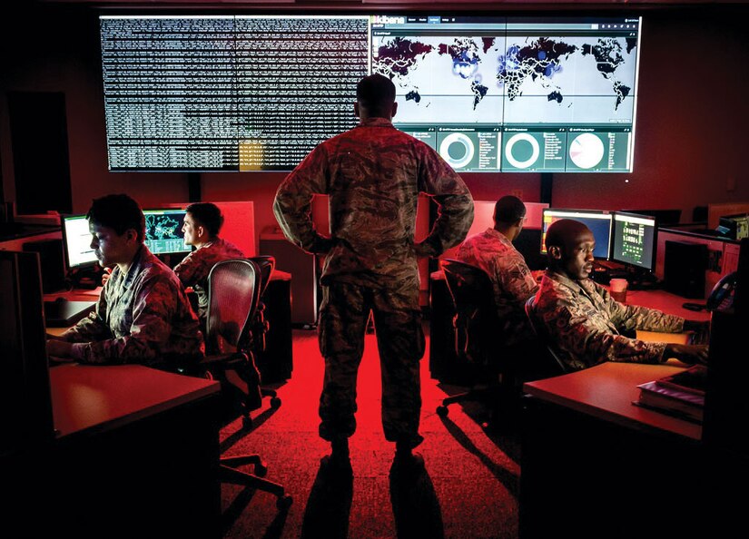 A cyber warfare operations officer reviews visualization data as analysts review log files and provide a cyber threat update.