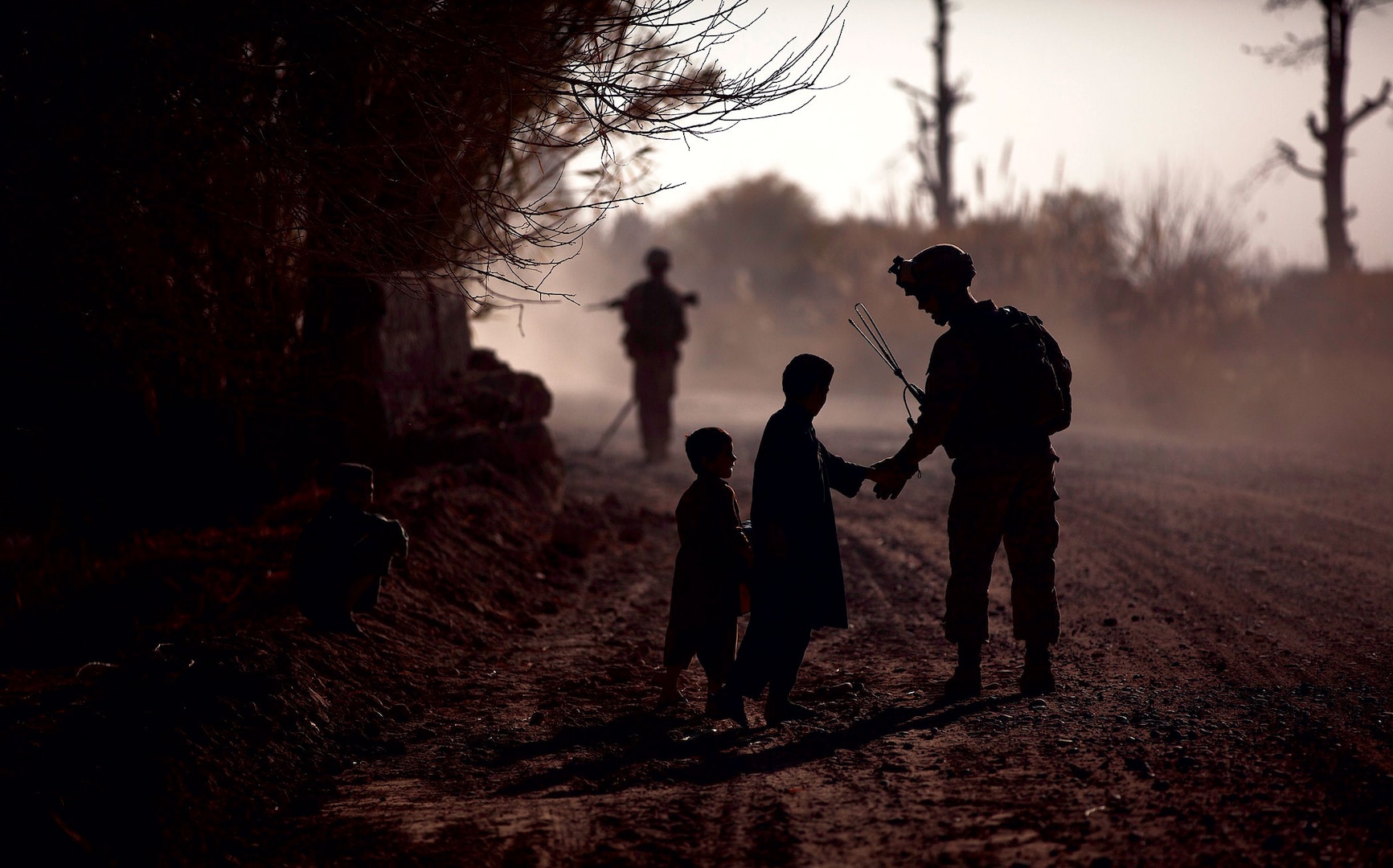 In 2011, a U.S. marine greets local children during a partnered security patrol with Afghan National Army soldiers in Helmand Province, Afghanistan. The marines aided Afghan National Security Forces in assuming security responsibilities; their interoperability is designed to further the expansion of stability, development, and legitimate governance by defeating insurgent forces and helping to secure the Afghan people. (DOD)