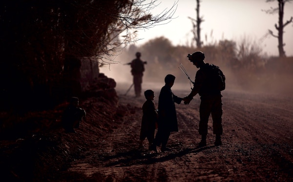 In 2011, a U.S. marine greets local children during a partnered security patrol with Afghan National Army soldiers in Helmand Province, Afghanistan. The marines aided Afghan National Security Forces in assuming security responsibilities; their interoperability is designed to further the expansion of stability, development, and legitimate governance by defeating insurgent forces and helping to secure the Afghan people. (DOD)