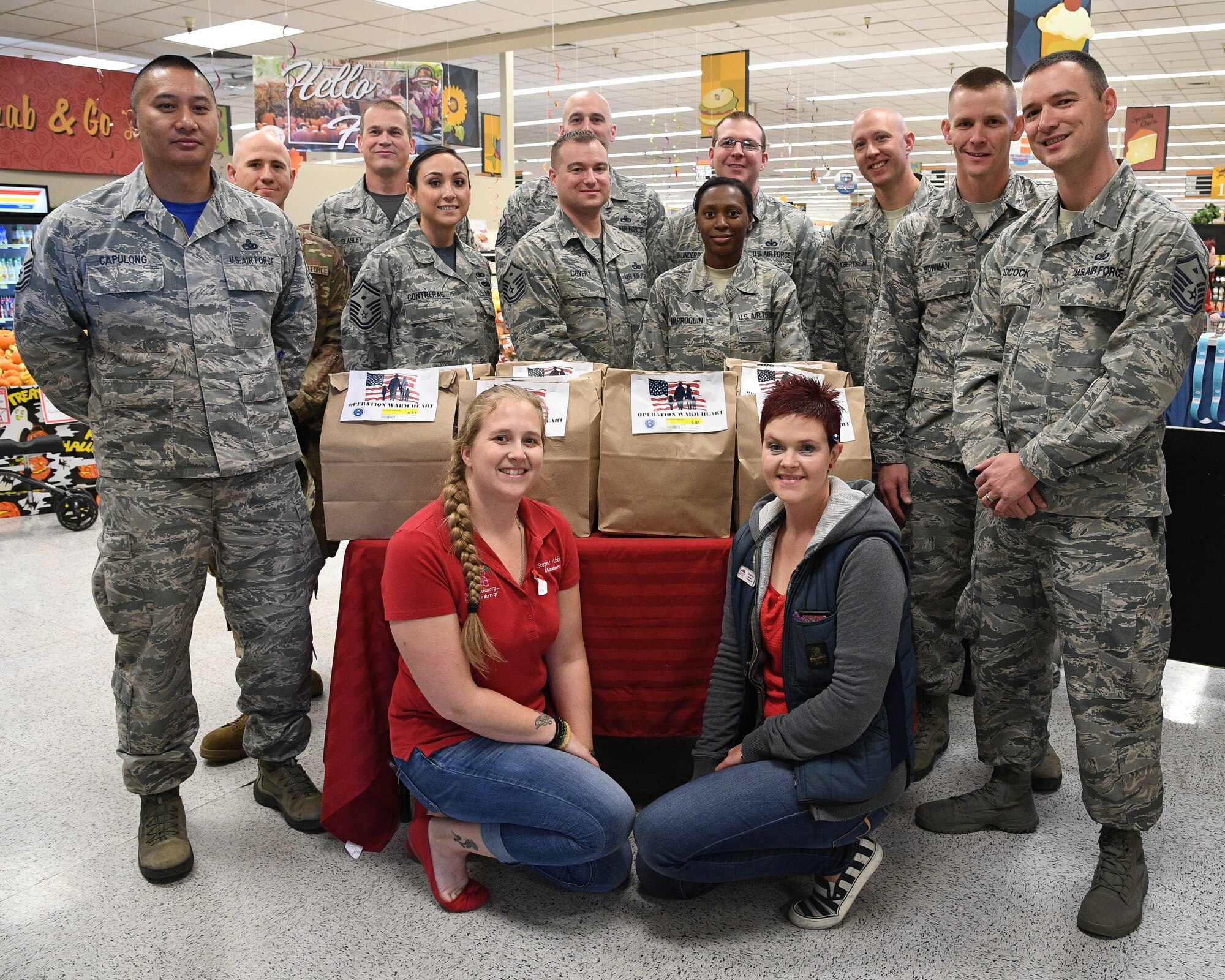Stephanie Abbey, left, Shannon Loftus and members of Hill's First Sergeant Council pose for a group photo around a table of Operation Warm Heart Thanksgiving bags on Nov. 2, 2108, at Hill Air Force Base, Utah. The First Sergeant Council and the commissary packaged 200 bags of Thanksgiving side dishes to be sold at cost to benefit Airmen during the upcoming holiday. Commissary patrons purchase the bags which are then delivered to Airmen along wth a turkey, potatoes and a pie that were donated by commissary vendors. (U.S. Air Force photo by R. Nial Bradshaw)