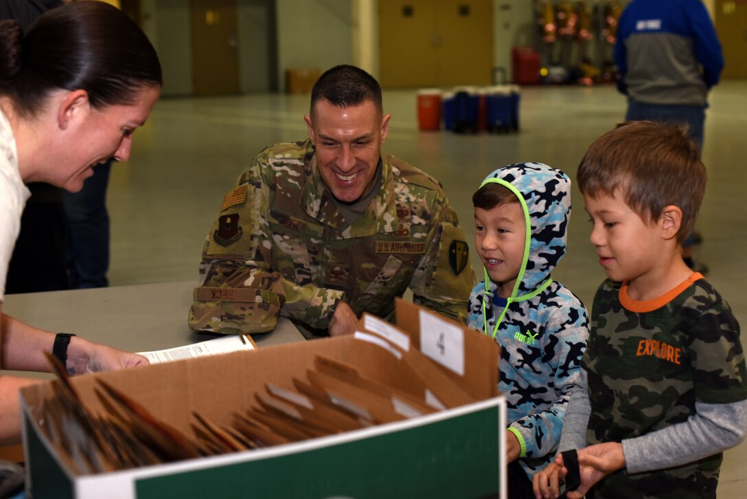 U.S. Air Force Col. Jason Beck, 17th Mission Support Group commander, helps his children with receiving their welcome packet and equipment at the processing line during the Operation KIDS event in the Louis F. Garland Department of Defense Fire Academy at Goodfellow Air Force Base, Texas, Nov. 3, 2018. As a part of the experience the children had to go through the processing line and receive medical and dental clearances before waiting with their group to go to the other events. (U.S. Air Force photo by Airman 1st Class Seraiah Hines/Released)