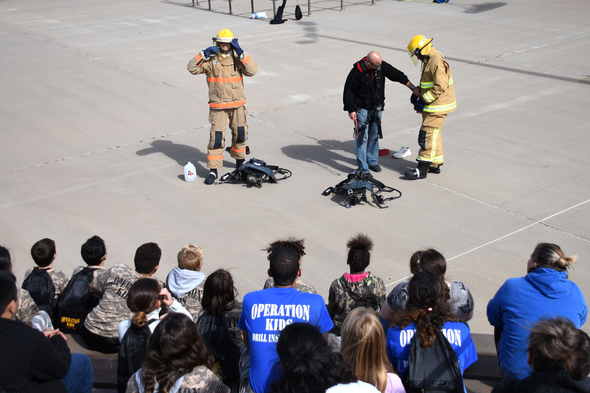 Members of the Louis F. Garland Department of Defense Fire Academy demonstrate how quickly firemen are to get suited up in case of an emergency to a group of Operation KIDS participants at the Louis F. Garland Department of Defense Fire Academy on Goodfellow Air Force Base, Texas, Nov. 3, 2018. After receiving the demonstration, the children were able to explore some of the fire trucks and witness them shooting water at a stationary object. (U.S. Air Force photo by Airman 1st Class Seraiah Hines/Released)