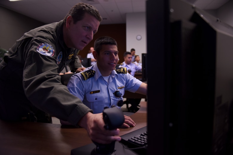 A South American fighter pilot and liaison to the U.S. Air Force shows a cadet from a Latin American service academy proper stick control on an F-35A Lightning II simulator Oct. 31, 2018, at Luke Air Force Base, Ariz. The top two cadets from each of various Latin American air service academies visited Luke as a part of the Department of Defense Latin American Cadet Initiative program. (U.S. Air Force photo by Senior Airman Ridge Shan)