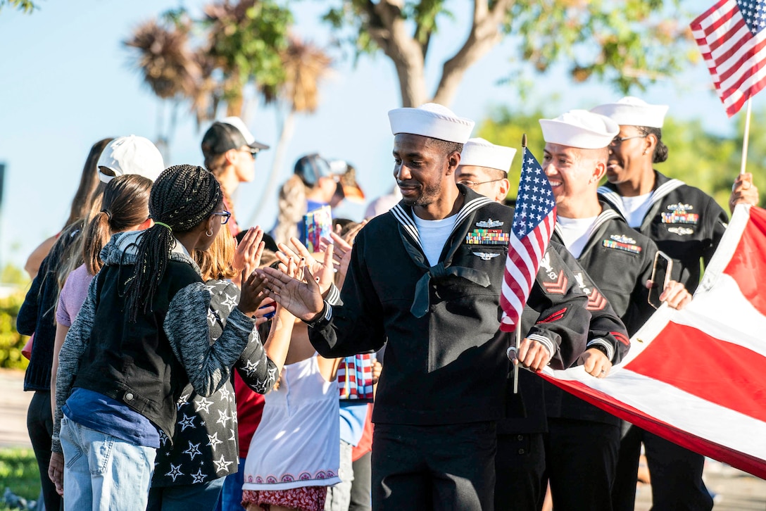 A sailor holding an American flag high-fives parade spectators.
