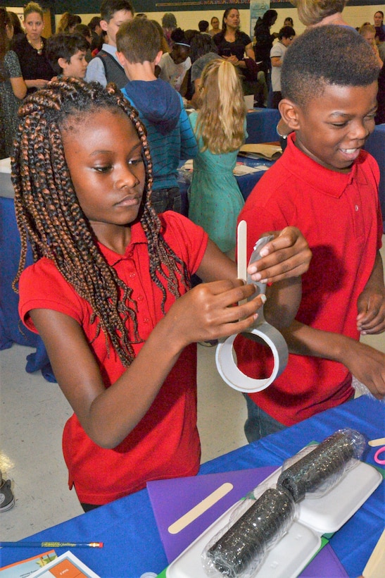 children are putting together and floating bridge using a piece of duct tape and a popsicle stick