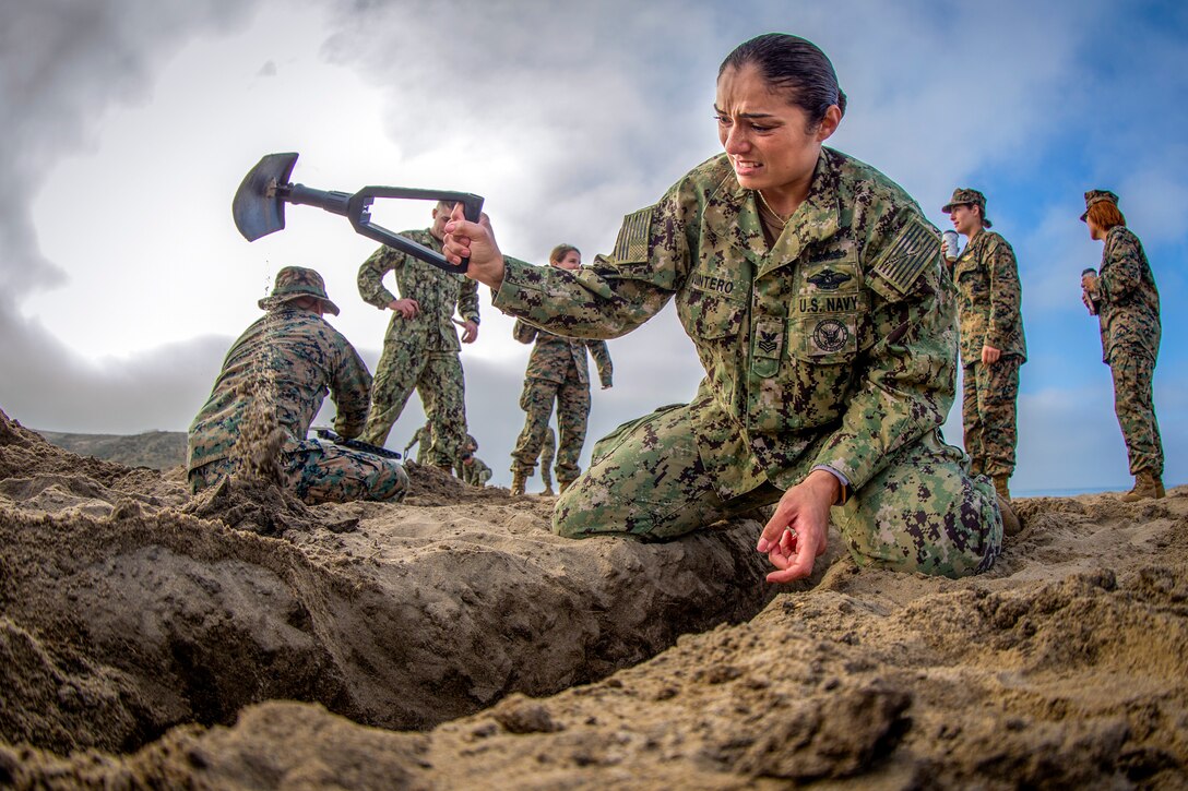 A sailor digs a trench with a foldable shovel.