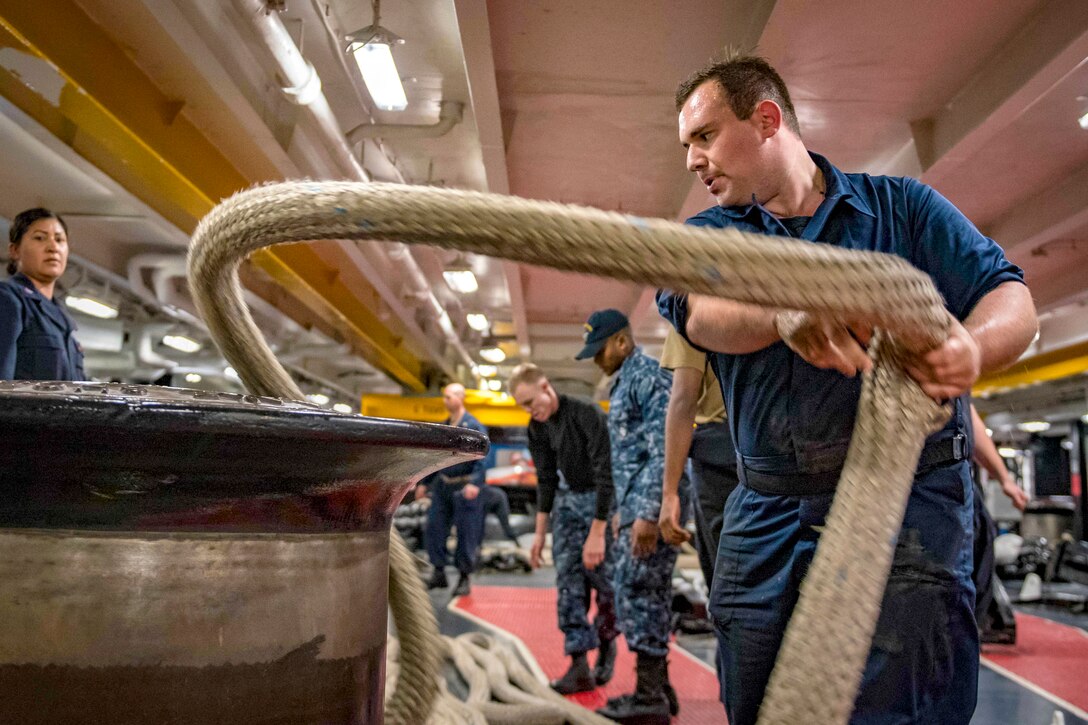A sailor wraps a whip around a capstan.