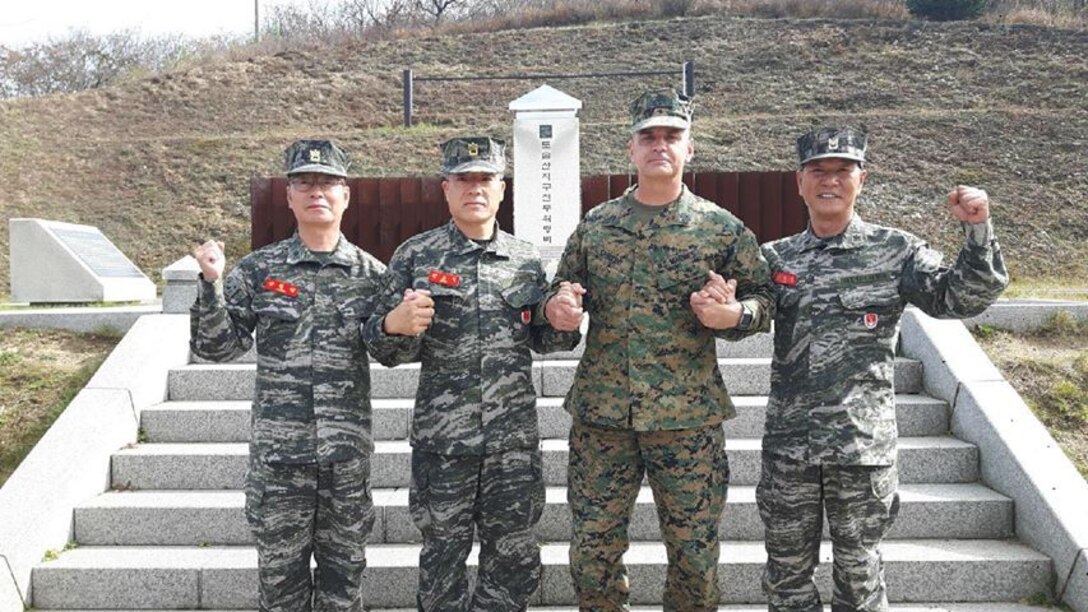 DOSOL MOUNTAIN, Republic of Korea – Sgt. Maj. Michael Saucedo (center right), sergeant major of U.S. Marine Corps Forces Korea, with Sgt. Maj. Yang, Byung Jang (left), 1st R.O.K. Marine Division sergeant major, Sgt. Maj. Jeon, Jong Ik (center left), R.O.K. Marine Corps sergeant major, and Sgt. Maj. Lee, Hwai Woo (right), 2nd R.O.K. MARDIV sergeant major, hold hands in solidarity in front of the battle memorial of Dosol Mountain to symbolize the strength of our alliance here. Dosol Mountain is where U.S. and R.O.K. Marines who fought in the Korean War earned the nickname “Mujuk”, which means invincible. The U.S. Marine Corps base in Pohang, South Korea was named Camp Mujuk to reflect this honor bestowed on them by the people of the R.O.K. (courtesy photo/Released)