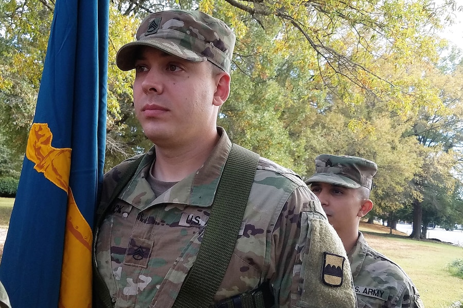 A sergeant stands next to flag