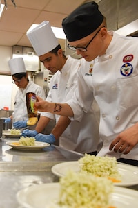 U.S. Army Sgt. Ethan Flagg, a 2nd Battalion, 377th Parachute Field Artillery Regiment culinary noncommissioned officer and Joint Culinary Institute instructor places honey on an orange tarragon salad during the grand opening lunch for JCI operated at the Gold Rush Inn. JCI is a new bi-monthly, two-week course, providing 10 food-service members from any military branch an opportunity to experience in-depth courses relating to the profession.