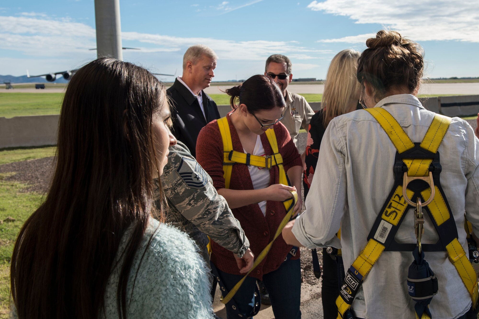 Military spouses from the 97th Air Mobility Wing put on harnesses to board a cherry picker lift during the Heartlink Spouse Orientation,