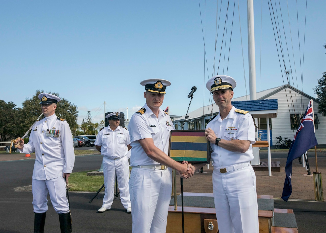 Chief of Naval Operations Adm. John M. Richardson and an Australian sailor hold a framed striped pennant.