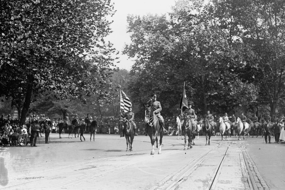 Troops on horseback parade down a street.