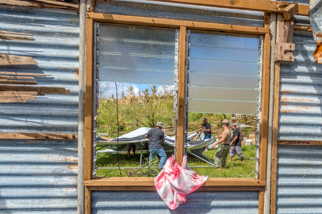 Sailors build a tent while surrounded with debris.