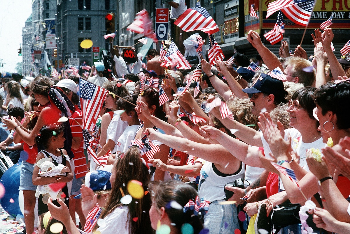 Onlookers wave flags and cheer on a city street.