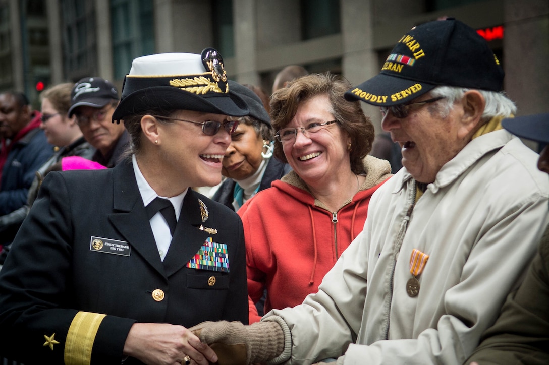 A sailor shakes hands with a veteran at a parade.