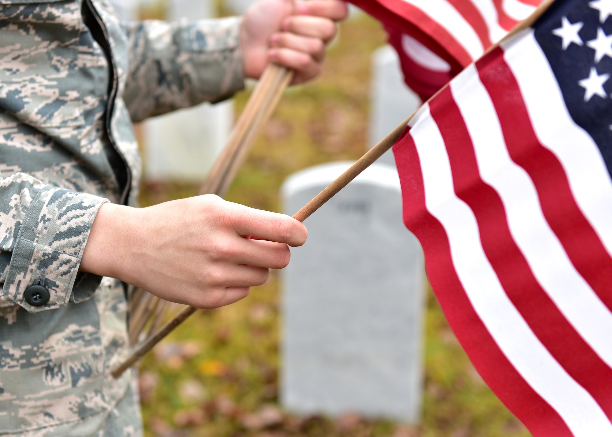 Individuals in uniform lay flags at graves of service members.