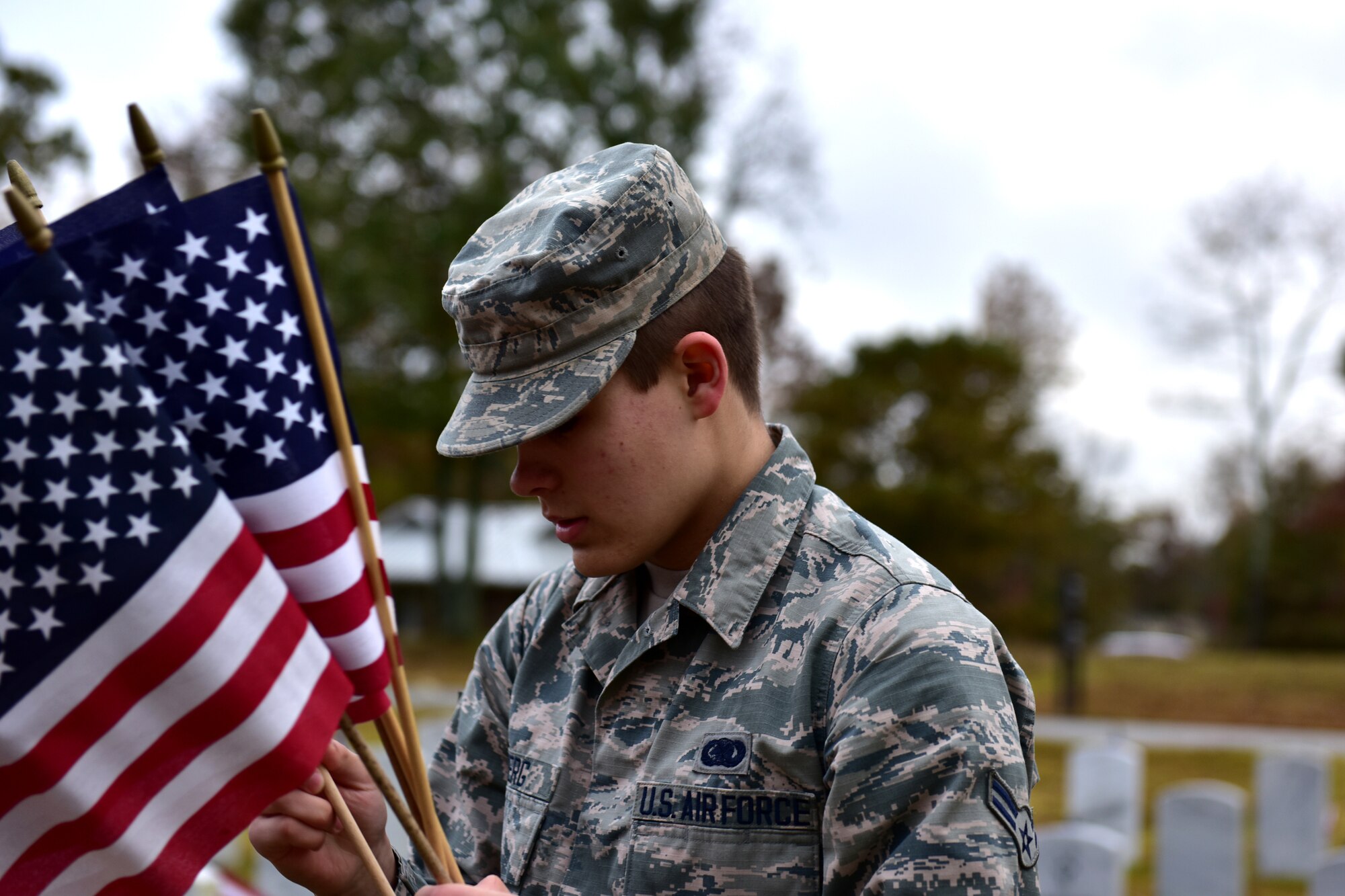 Individuals in uniform lay flags at graves of service members.