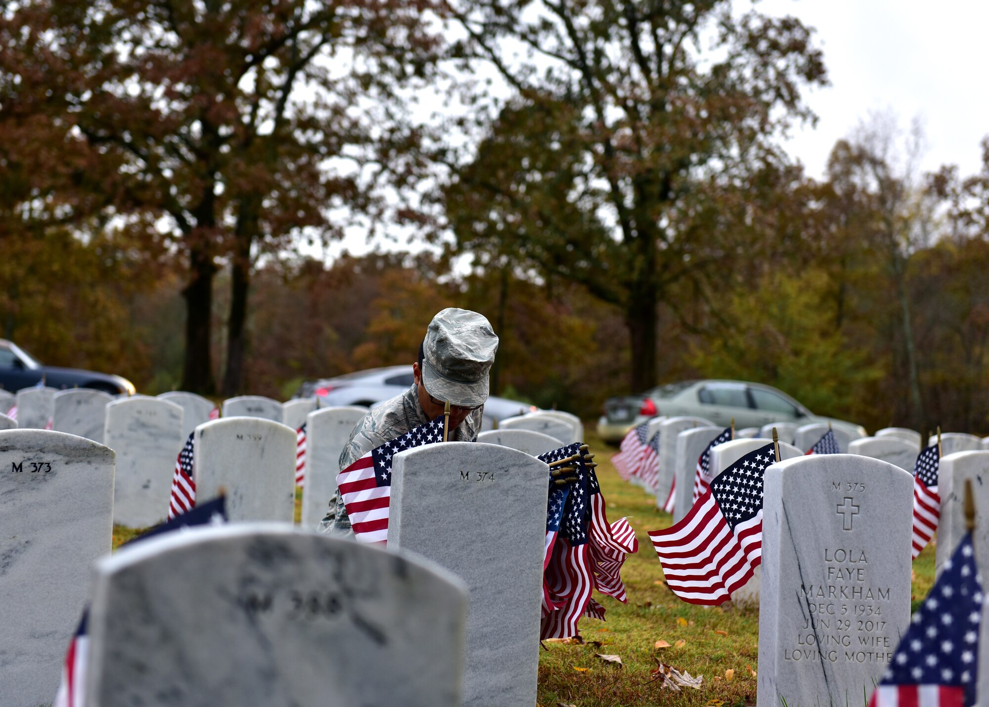 Individuals in uniform lay flags at graves of service members.