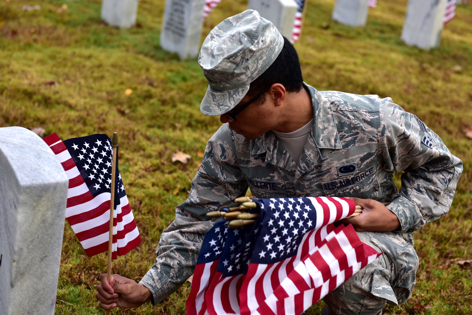 Individuals in uniform lay flags at graves of service members.