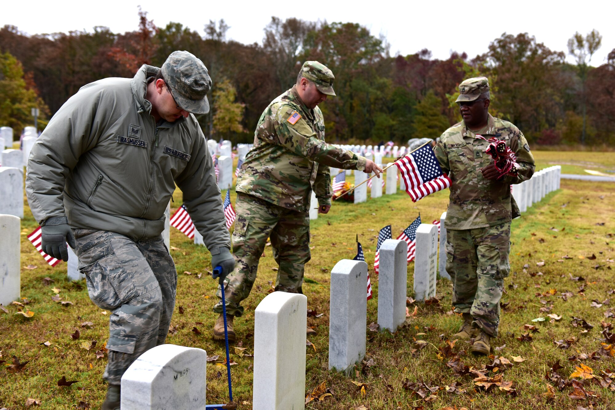 Individuals in uniform lay flags at graves of service members.