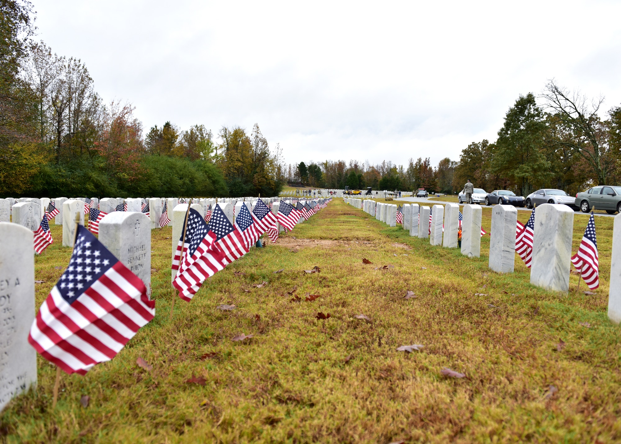 Individuals in uniform lay flags at graves of service members.