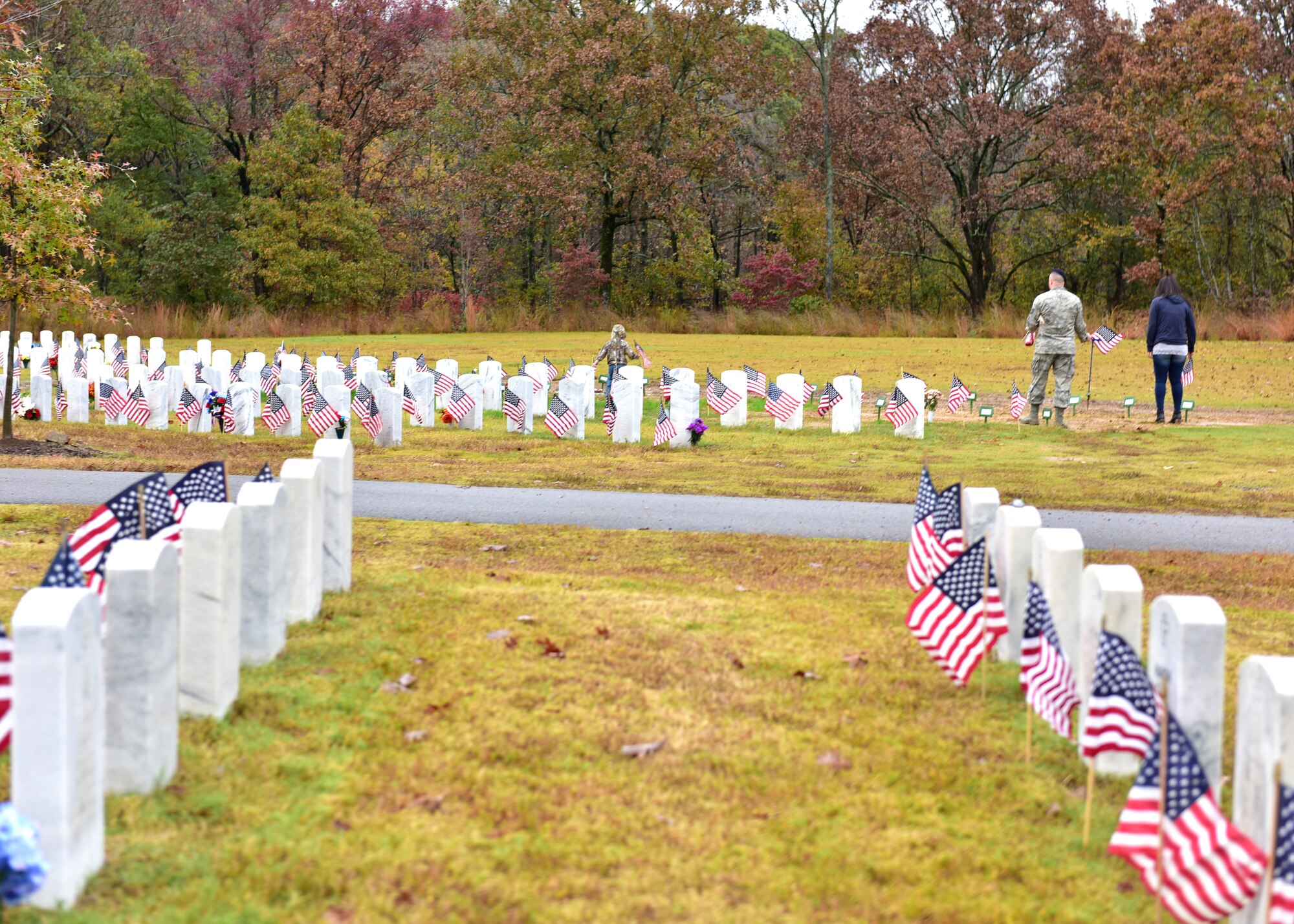 Individuals in uniform lay flags at graves of service members.