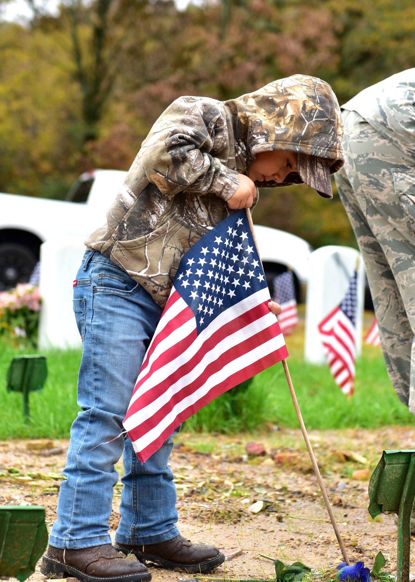 Individuals in uniform lay flags at graves of service members.