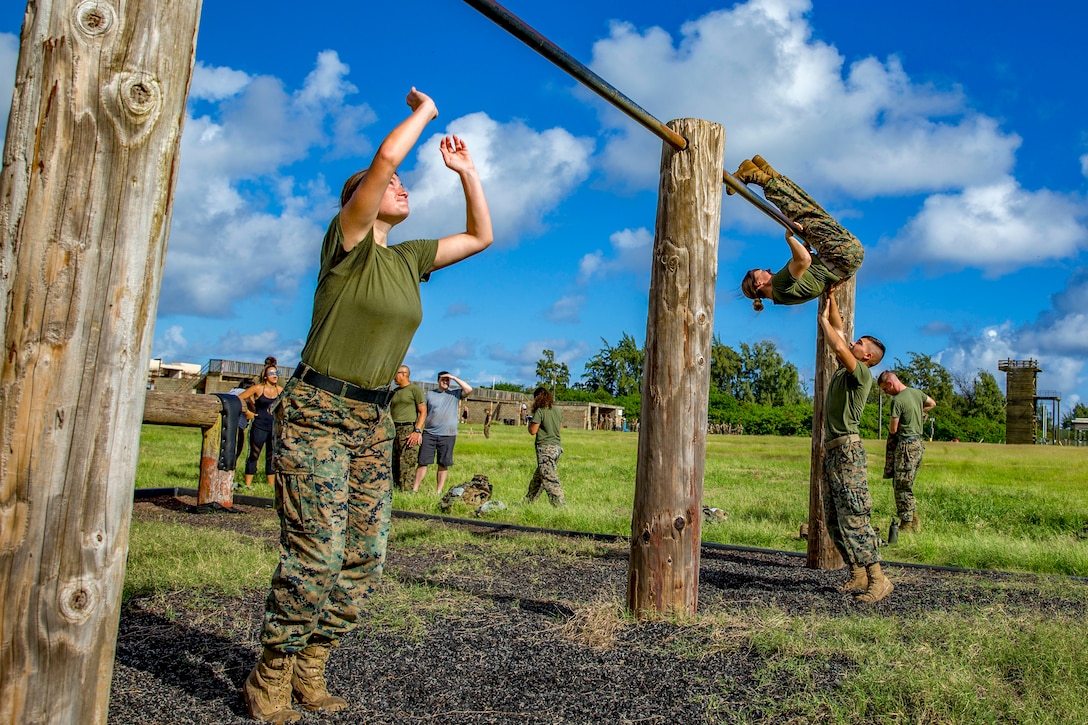 Marine spouses grab an overhead bar obstacle on an outside obstacle course.