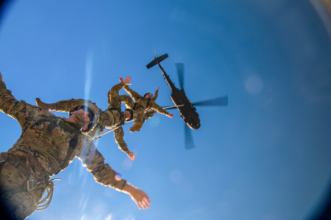 Soldiers hang on a rope attached to a helicopter.