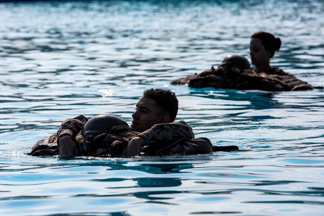 Two marines swim carrying gear.