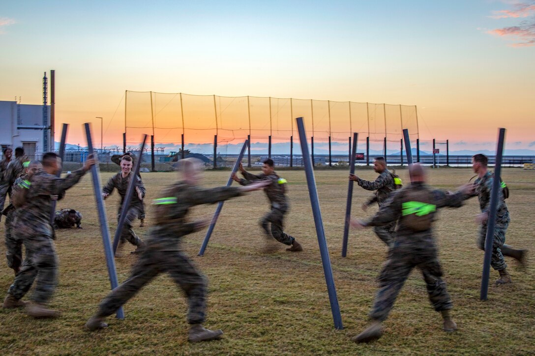 Marines and sailors stand in a circle and pass long poles between each other.
