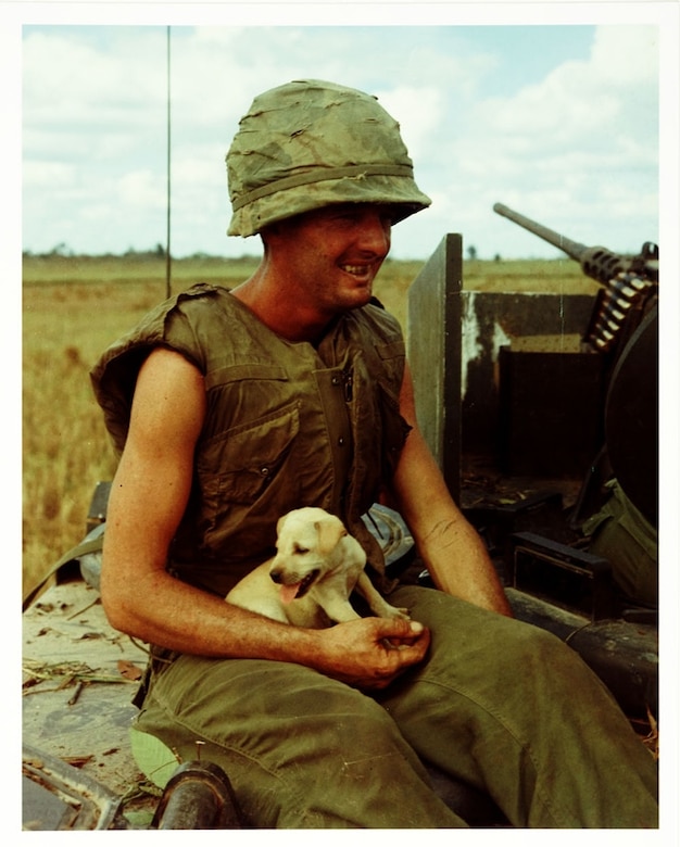 A soldier in South Vietnam sits smiling with puppy in his lap.