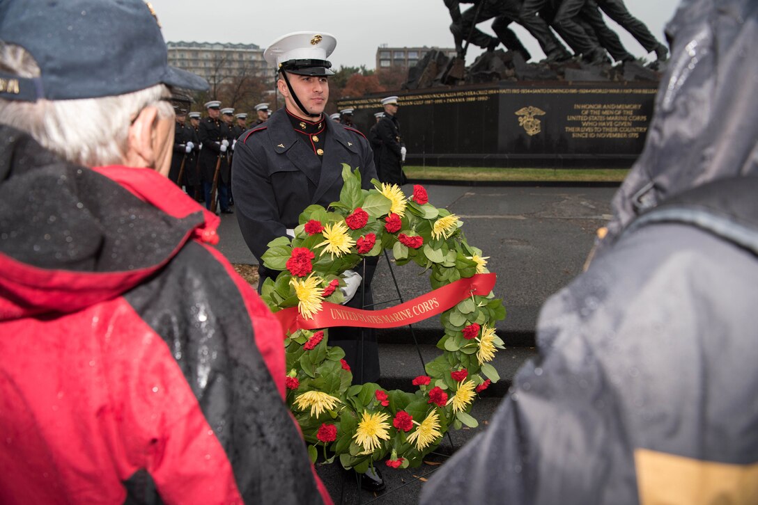 A Marine stands behind a wreath in front of the Marine Corps War Memorial.