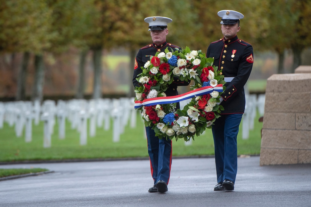 Two U.S. Marines carry a wreath at a cemetery.