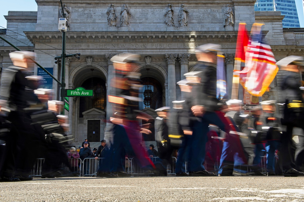 Spectators watch as a blur of Marines and sailors march past the New York Public Library.