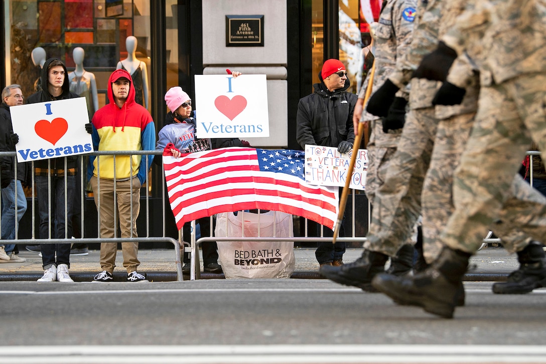 Spectators hold signs supporting veterans along the 2018 Veterans Day Parade route.