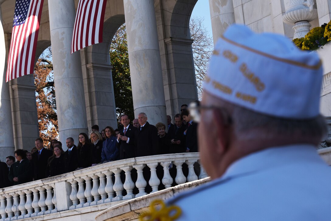 A veteran looks at the defense leaders standing on the balcony of the Memorial Amphitheater at Arlington National Cemetery