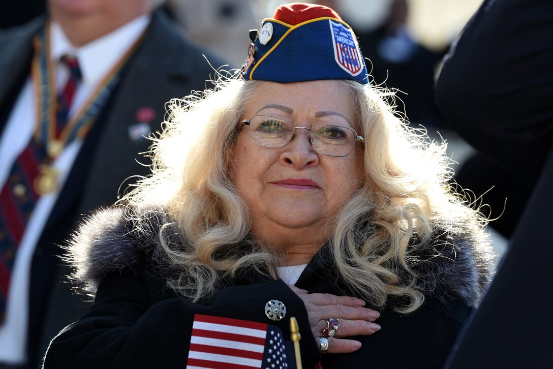 A woman holding a small American flag places her other hand over her heart.