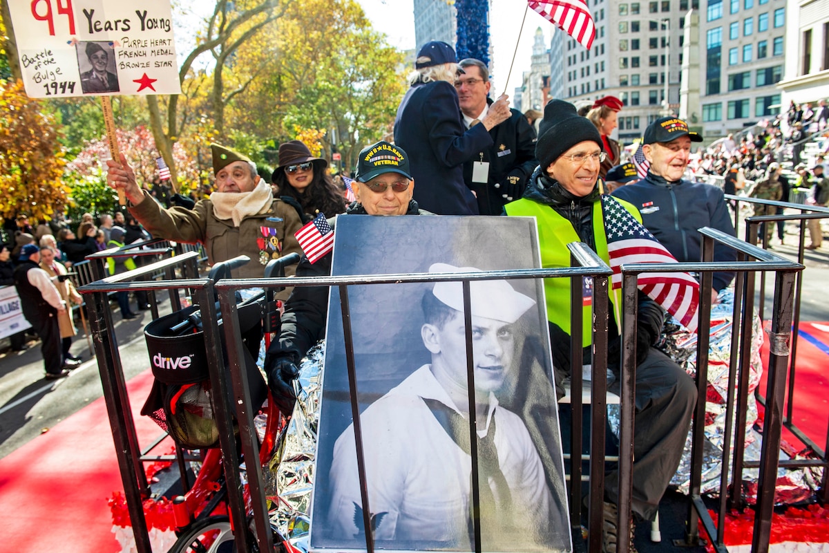 World War II veterans ride on a float during a parade while spectators watch.