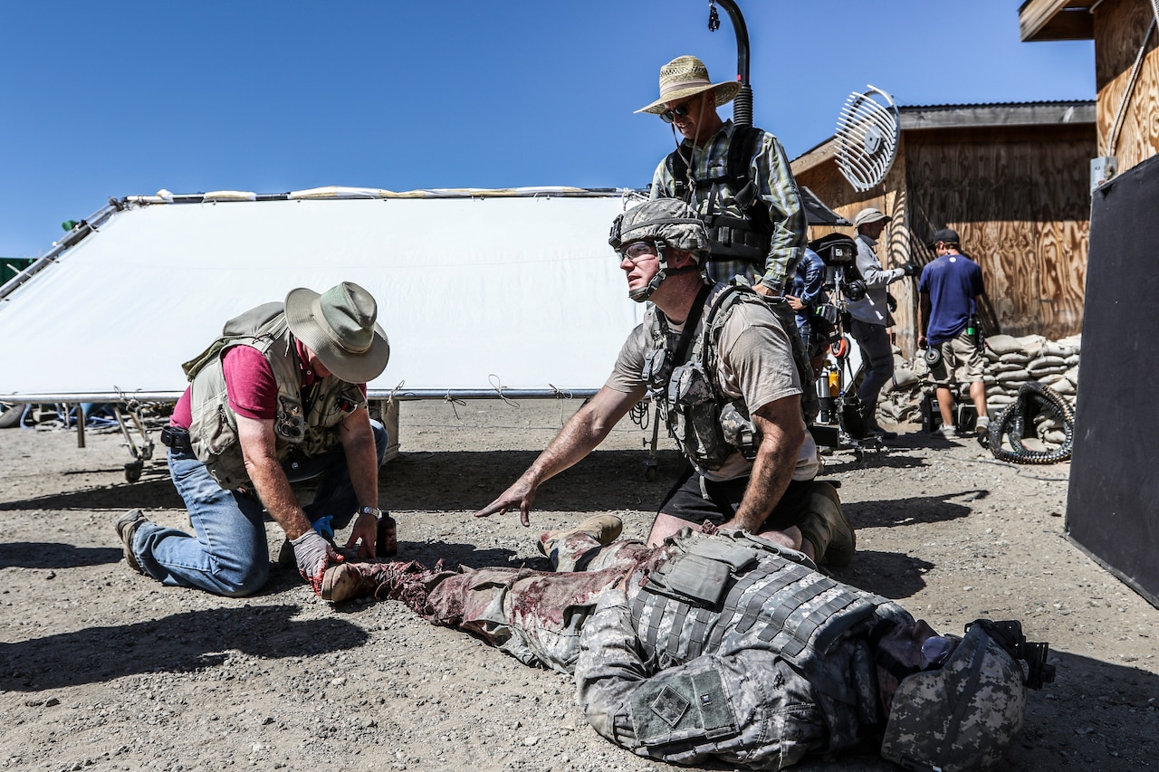 An actor kneels over a stuntman portraying an injured soldier.