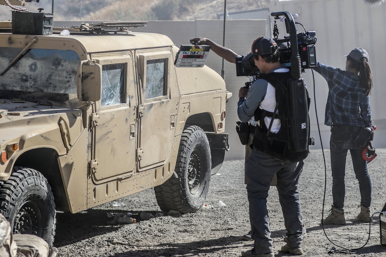 A camera operator films a slate at the start of a scene with a Humvee.