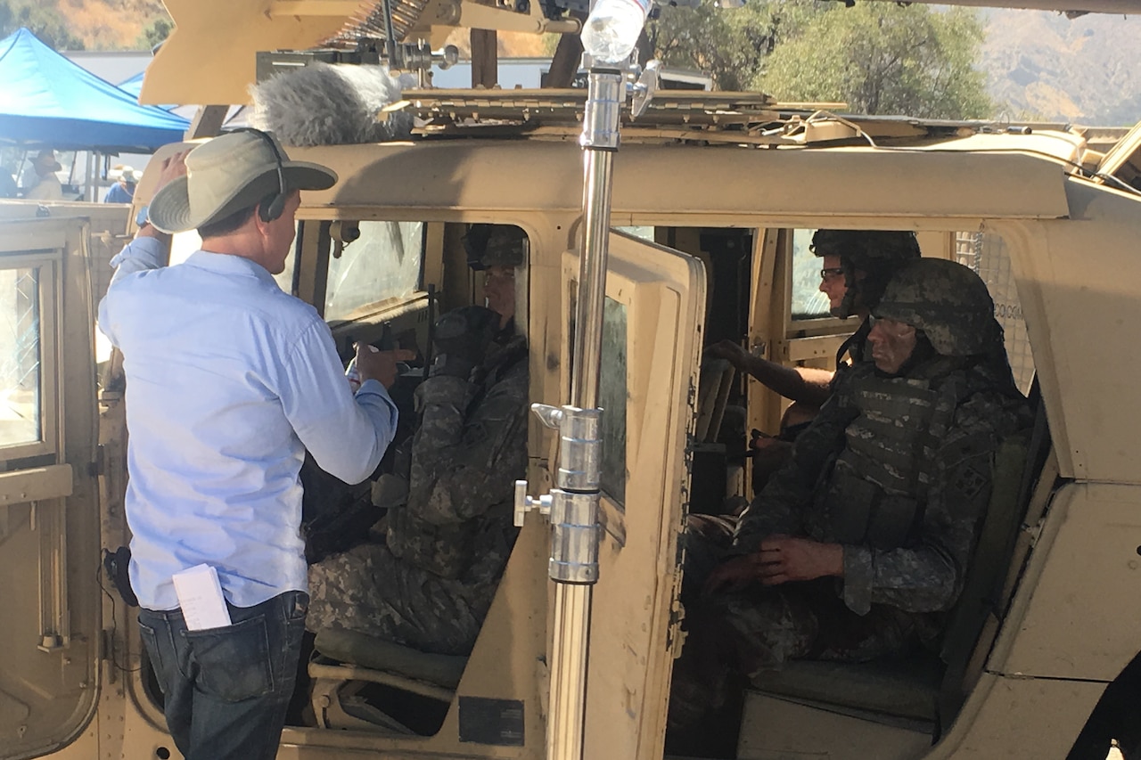 A director stands by a Humvee talking to actors inside portraying soldiers.