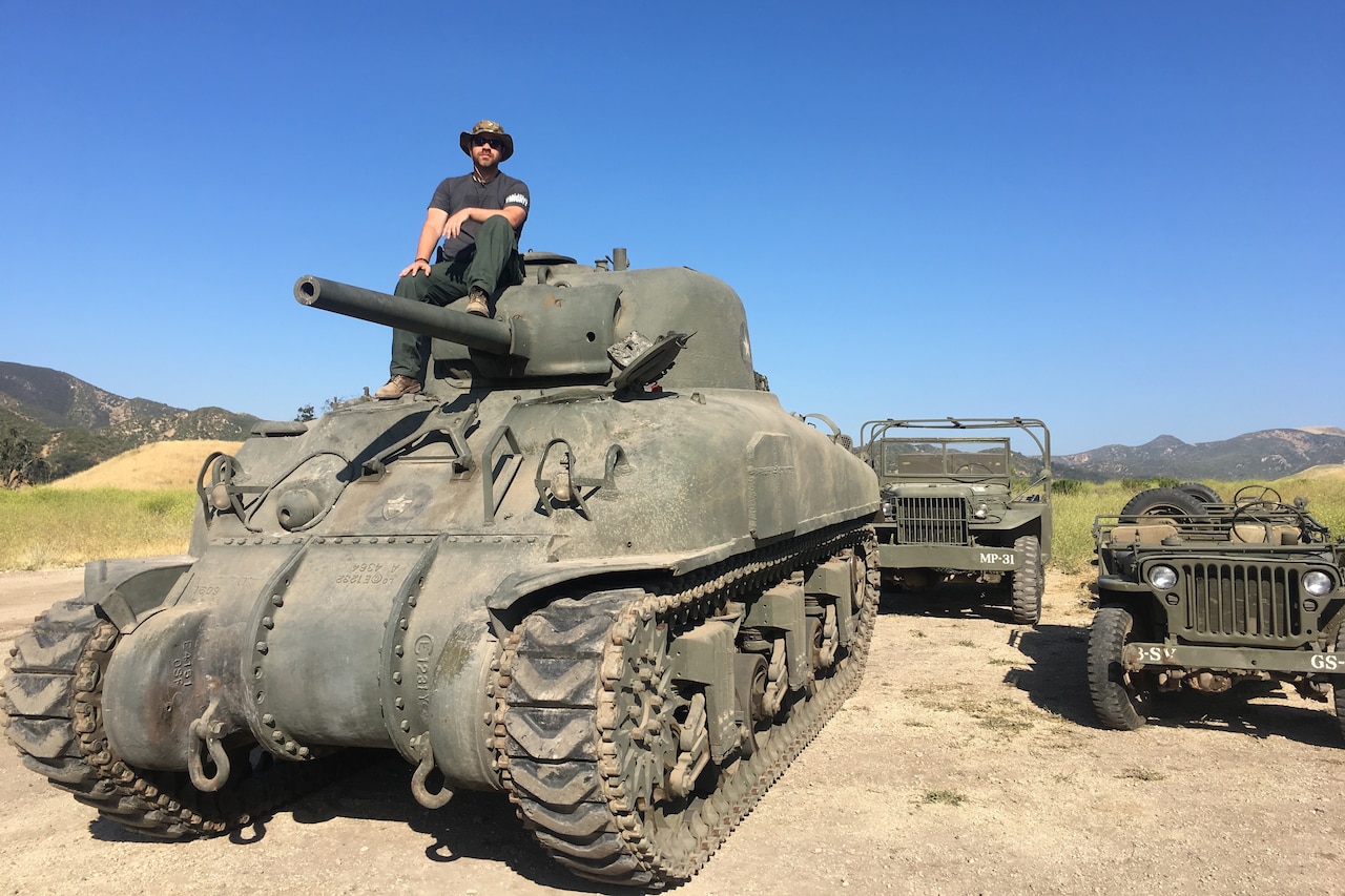 A man sits atop a WWII-era Army tank.