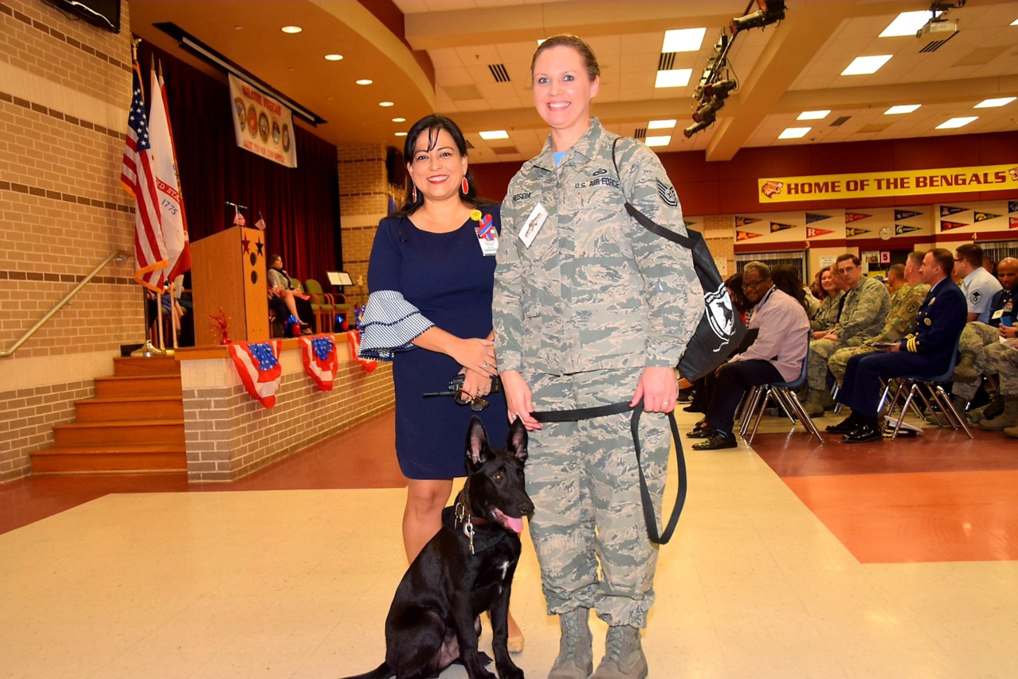 Christina Rather (left), principal at Dolph Briscoe Middle School in San Antonio, Texas, and Tech. Sgt. Melissa Proscia, 433rd Airlift Wing command post, and TThunder, a five-month old Belgian Malinois puppy from the Military Working Dog program at Joint Base San Antonio-Lackland, Texas, take a moment prior to the school’s 9th annual Veterans Day ceremony.