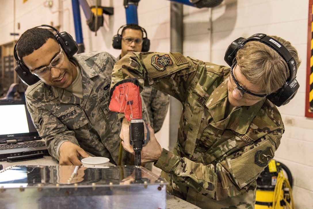 Airman 1st Class Reynaldo Rodriguez, right, 436th Maintenance Squadron aircraft structural maintenance journeyman, watches Gen. Maryanne Miller, left, Air Mobility Command commander, install a CherryMAX rivet on a simulated aircraft part Nov. 7, 2018, at Dover Air Force Base, Del. Miller installed the rivet during her tour of the Fabrication Flight. (U.S. Air Force photo by Roland Balik)